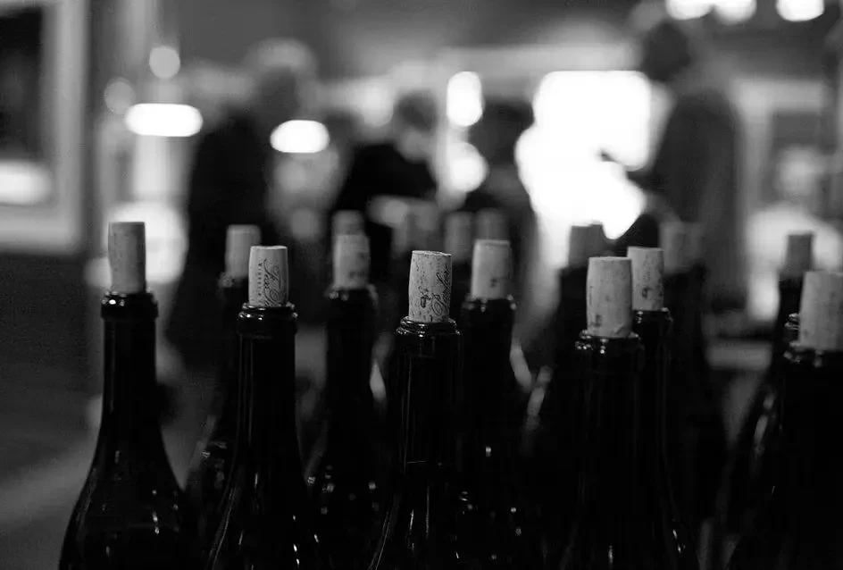 Black and white photo of wine bottle corks with blurred people.