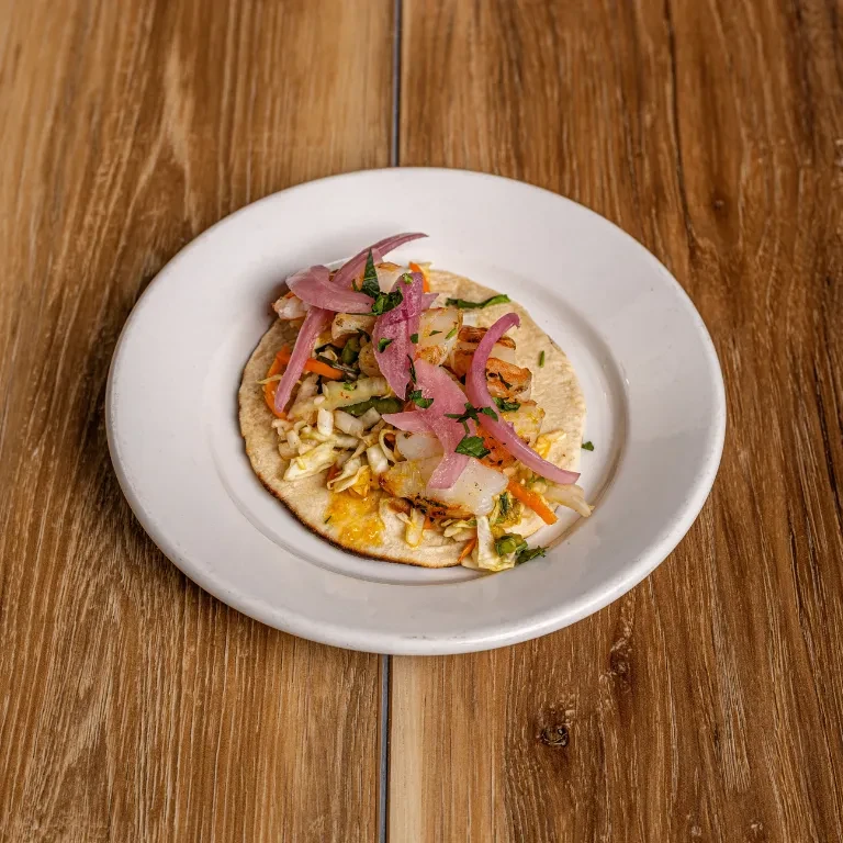 Shrimp street taco with pickled onions on a white plate.