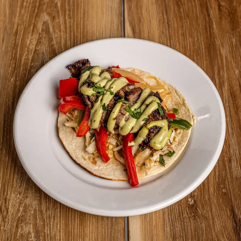 Single grilled meat taco with peppers, green sauce, and herbs.