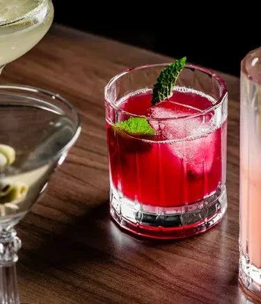 Close-up of a red mint cocktail and other drinks on dark wood.