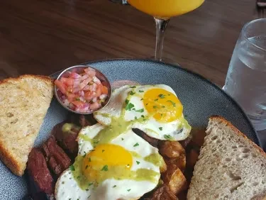 Close-up breakfast plate: sunny-side eggs, potatoes, seared meat, and toast.