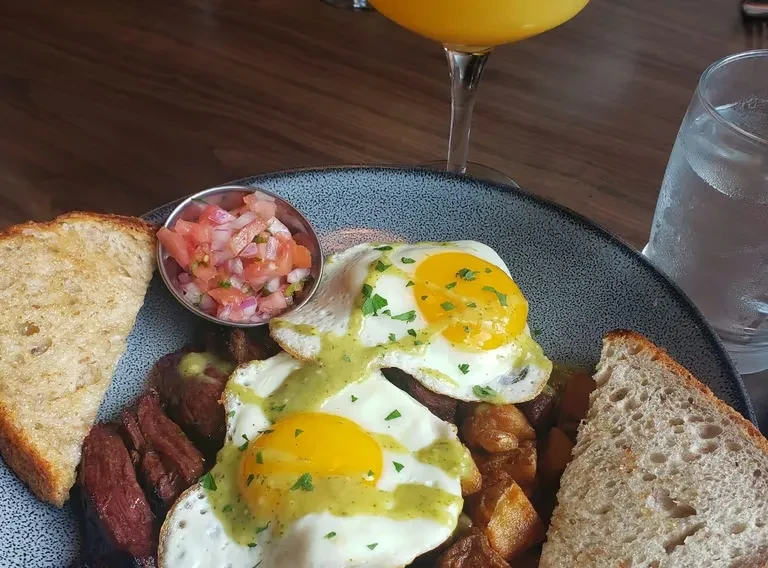 Hearty breakfast plate with sunny-side-up eggs, potatoes, meat, and pico de gallo.