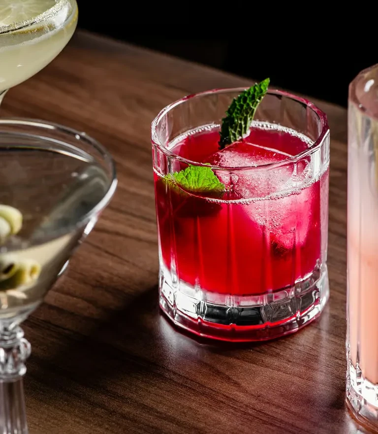 Close-up of various colorful cocktails on a polished dark wood surface.
