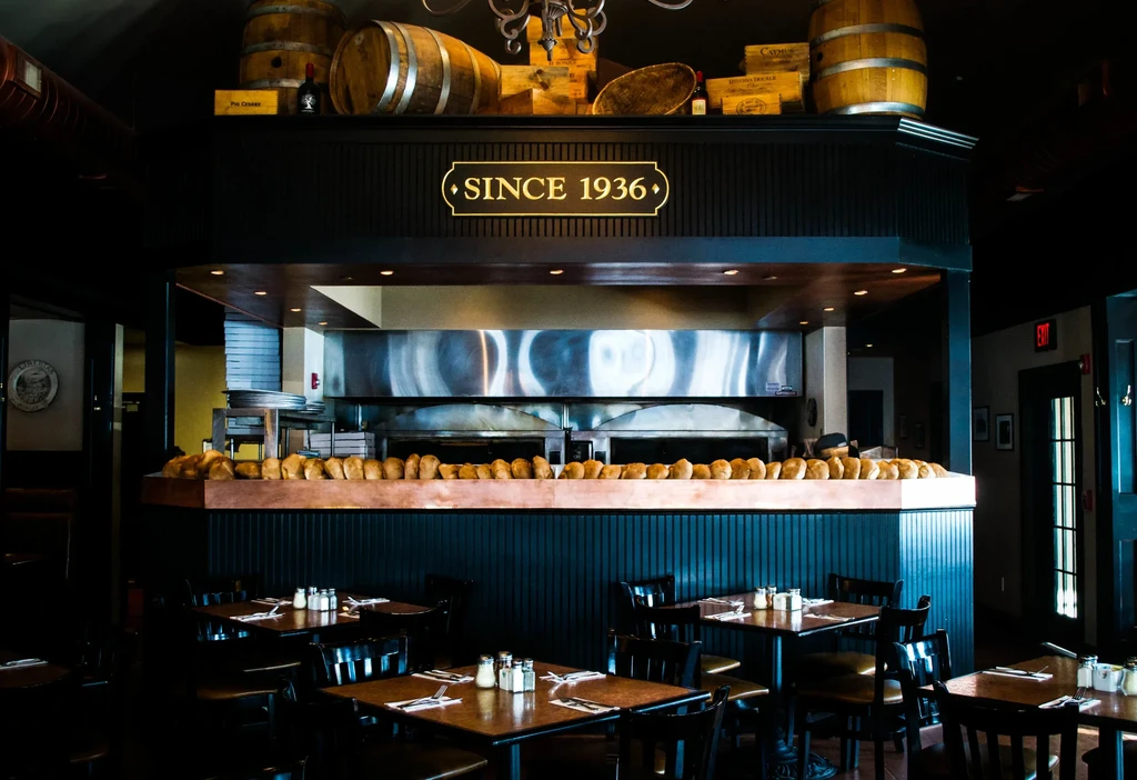 Restaurant interior: "SINCE 1936" sign, fresh bread loaves, and set tables.