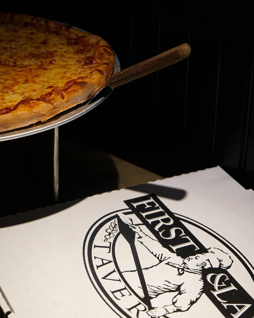 Close-up of freshly baked cheese pizza on pan with peel and box.