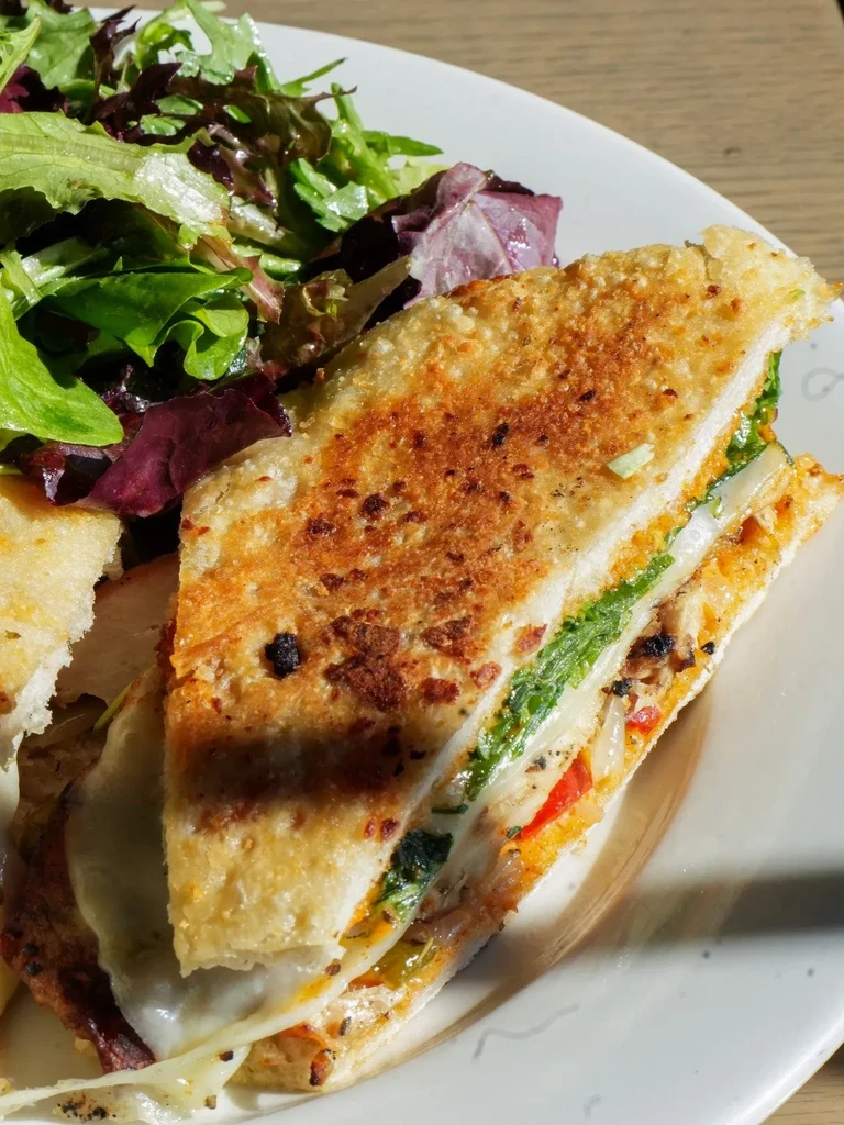 Grilled sandwich with melted cheese, greens, and a side salad.
