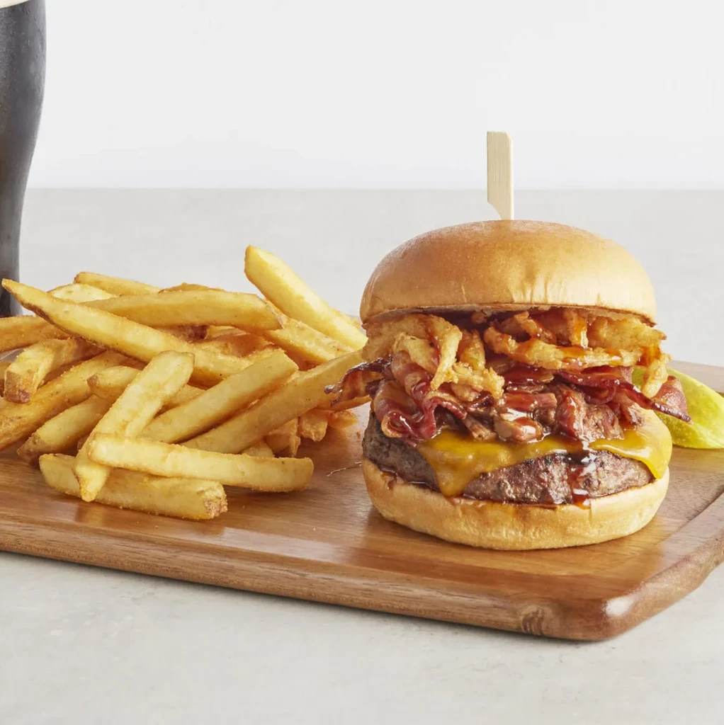 Cheeseburger with bacon, fried onions, and fries on a wooden board.