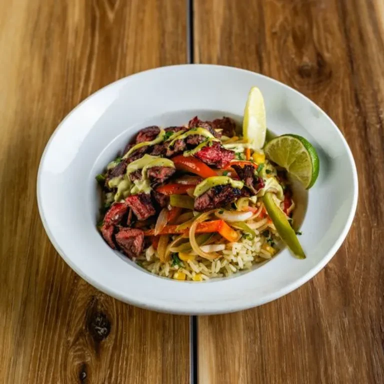 Close-up of grilled meat, rice, vegetables, green sauce, and lime.