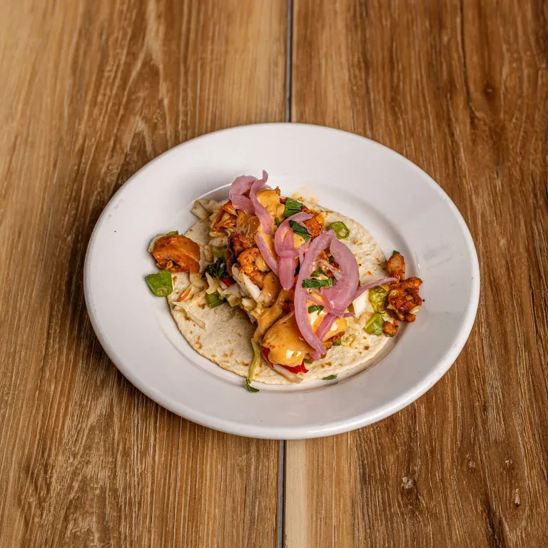 A colorful taco with grilled protein, slaw, and pink pickled onions.