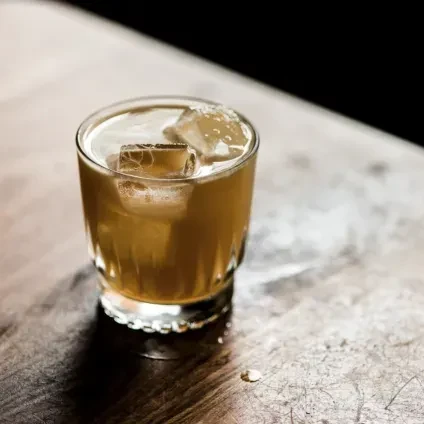 Amber cocktail with ice in a faceted glass on a wooden bar.