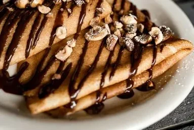 Crepes folded into triangles, drizzled with chocolate, nuts, and powdered sugar.