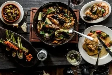 Overhead of a rustic table with paella, seafood, and Mediterranean dishes.