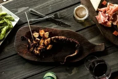 Cooked octopus, potatoes, meats, cheese, beer, and wine on a rustic table.