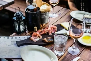 Rustic wooden table with charcuterie, wines, and a 'BARCELONA' menu.
