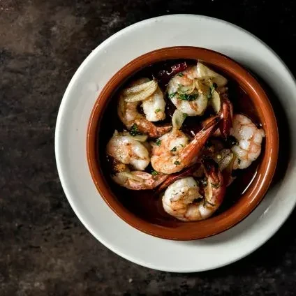 Sautéed shrimp with garlic, herbs, red pepper flakes in terracotta bowl.