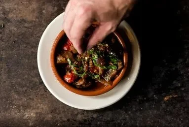 Rustic vegetable stew with tomatoes and herbs, garnished by a hand.