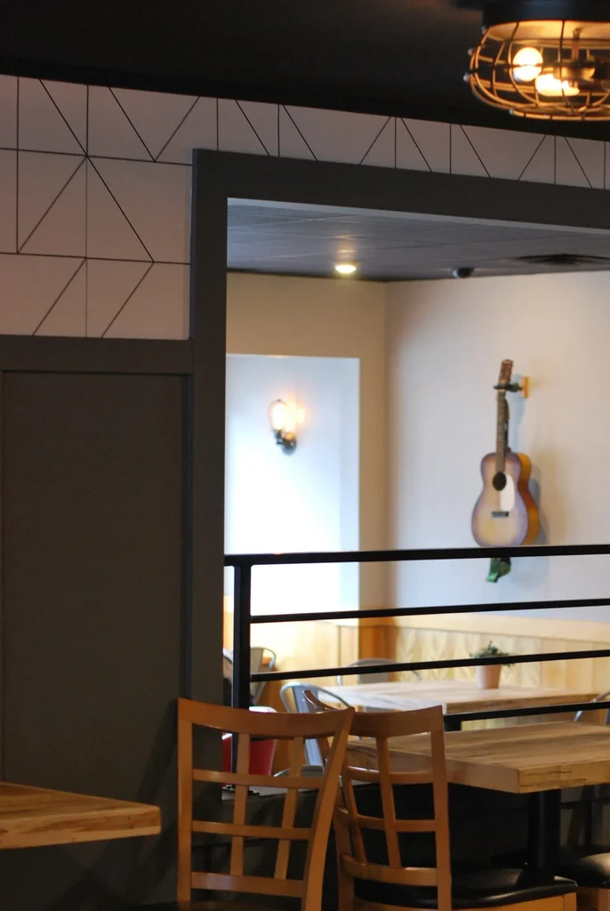 Restaurant interior: wooden chairs, patterned wall, archway, and guitar.