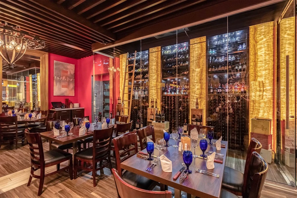 Upscale restaurant dining room, wooden tables, and large illuminated glass wine cellar.