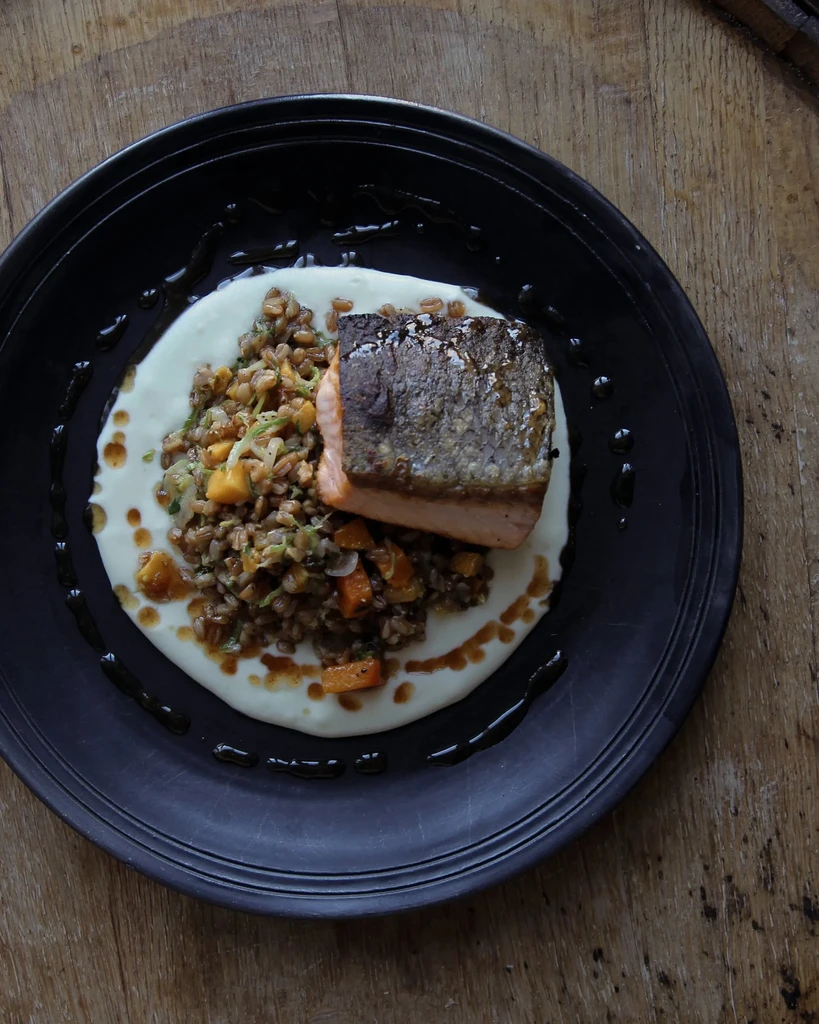 Plated seared salmon, grains, and two sauces on a rustic wood surface.