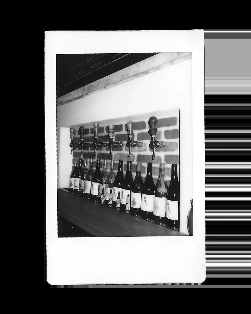 Black and white photo of bar taps on brick wall with bottles.