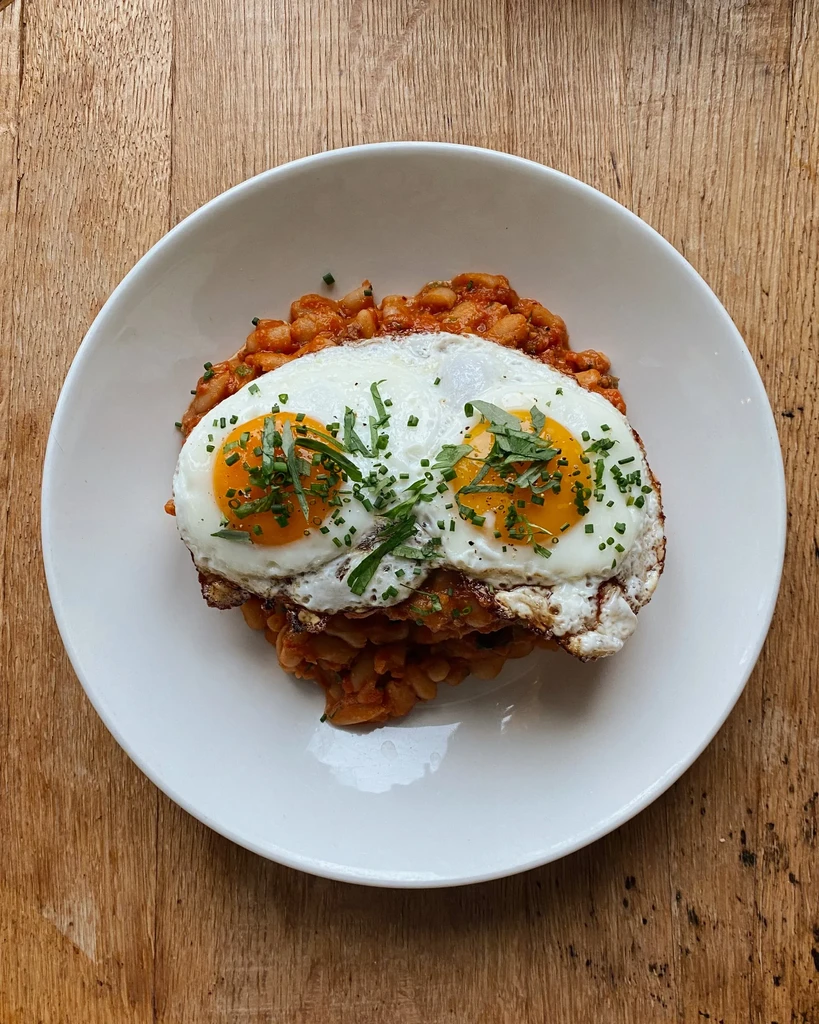 Close-up of baked beans with two runny fried eggs and chives.