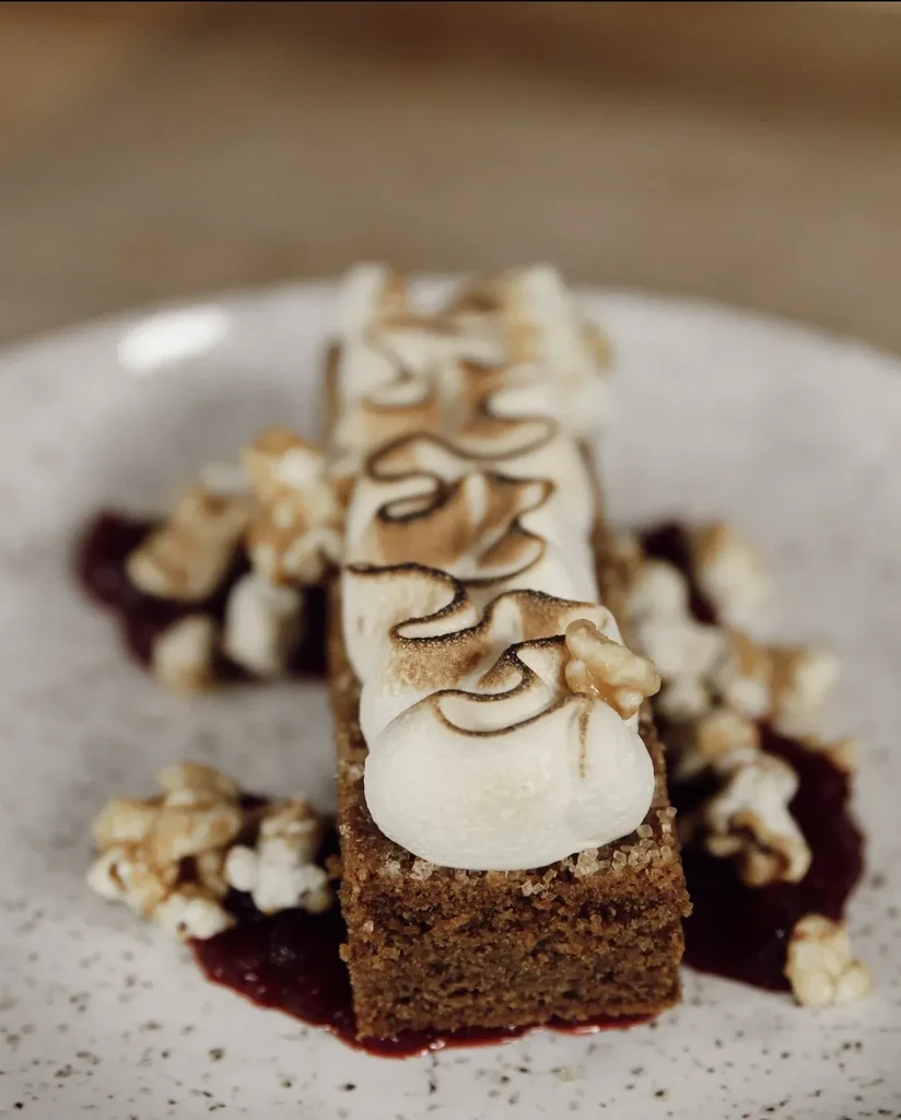 Rectangular cake with toasted meringue, popcorn, and red sauce.