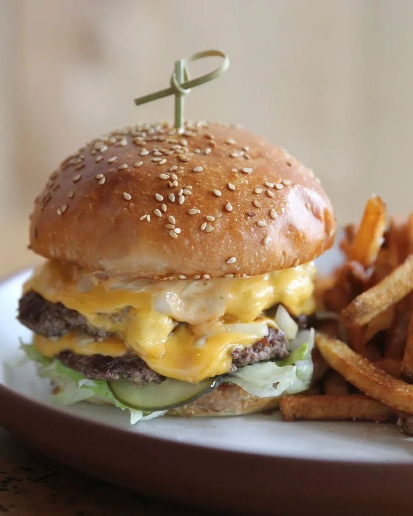 Double cheeseburger with melted cheese, lettuce, pickles, and french fries on a plate.
