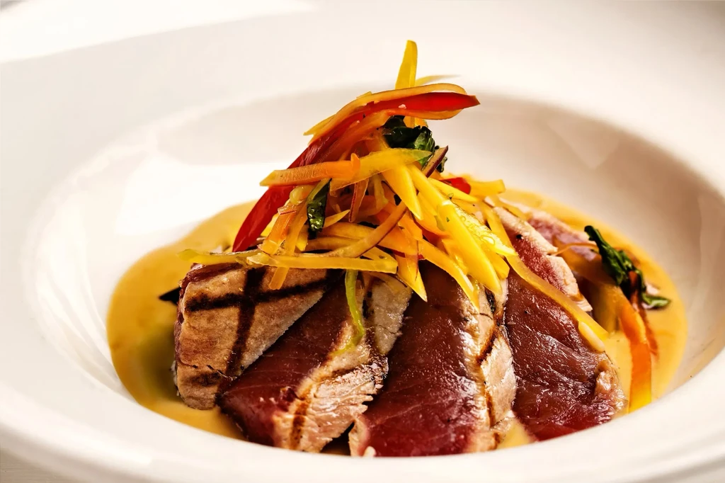 Seared tuna slices with creamy sauce and colorful julienned toppings.