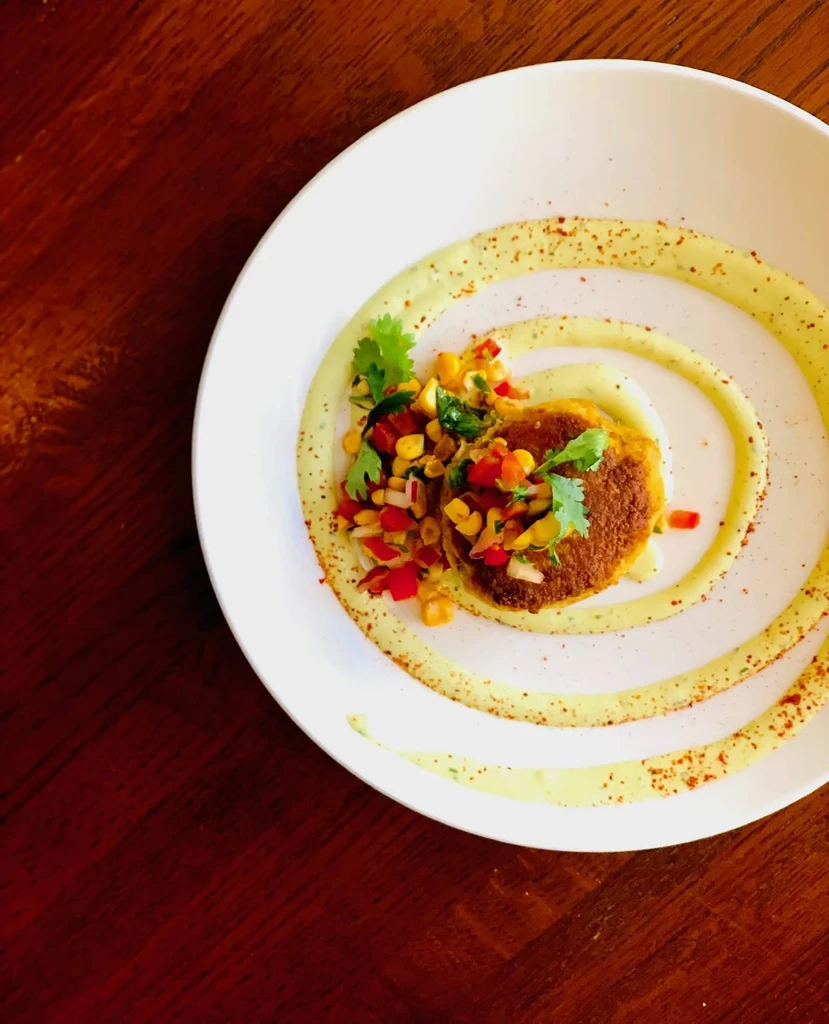 Golden-brown patty with colorful relish and sauce on white plate.