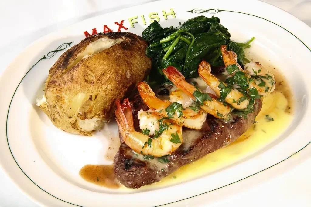 Grilled surf and turf meal with steak, shrimp, potato, and spinach.