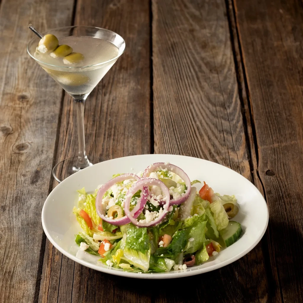 A clear martini and a fresh salad on a rustic wooden table.