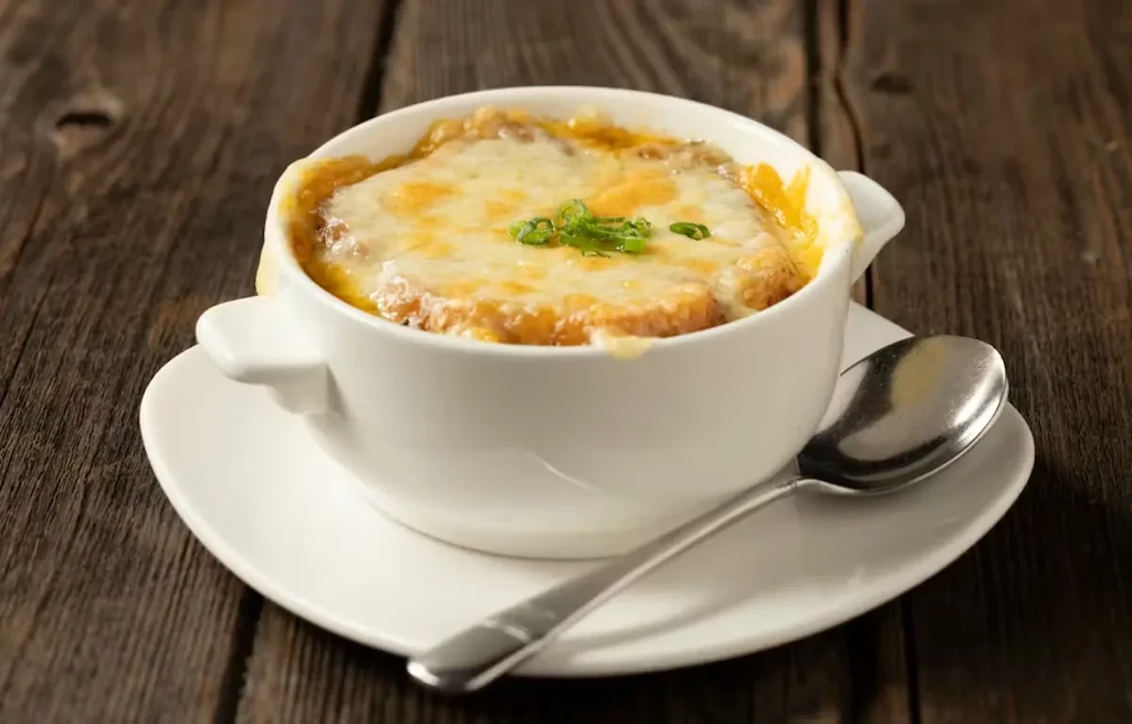Steaming French onion soup with melted cheese and chives on wood.