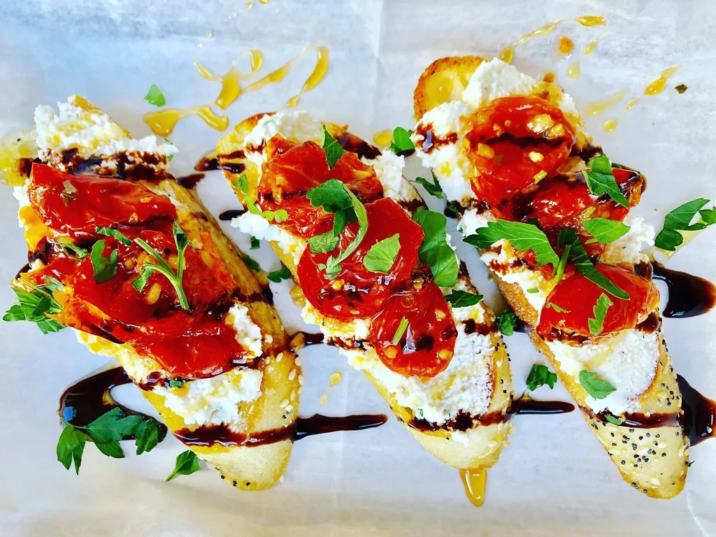 Three bruschetta with creamy cheese, roasted tomatoes, herbs, balsamic glaze.