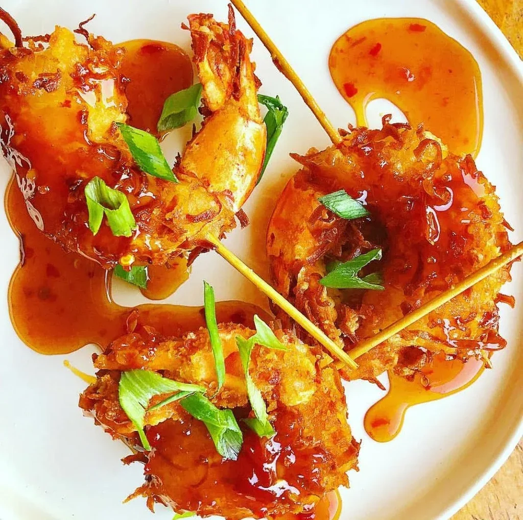 Crispy golden-battered shrimp skewers with orange sauce, green onions.