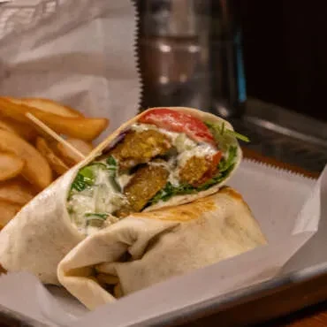Crispy falafel wrap halved with lettuce, tomatoes, sauce, and fries.