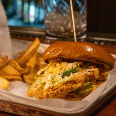 Gourmet fried chicken sandwich, coleslaw, pickles, and thick-cut fries on a tray.
