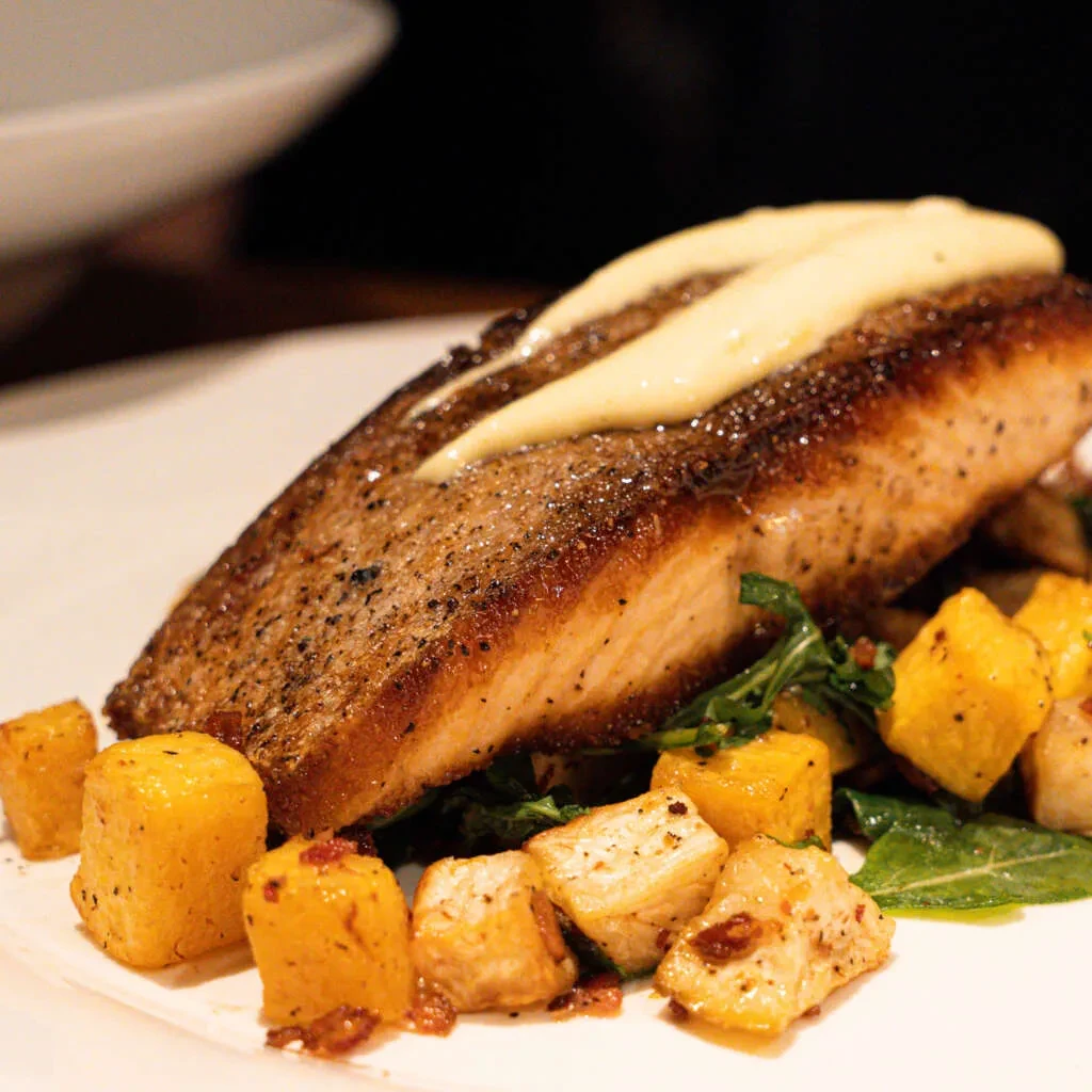 Salmon with crispy skin, creamy sauce, greens, and roasted vegetables.
