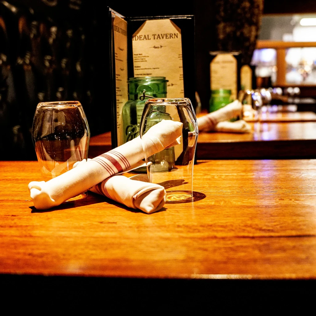 Rustic wooden table with glasses, napkins, and an "IDEAL TAVERN" menu.