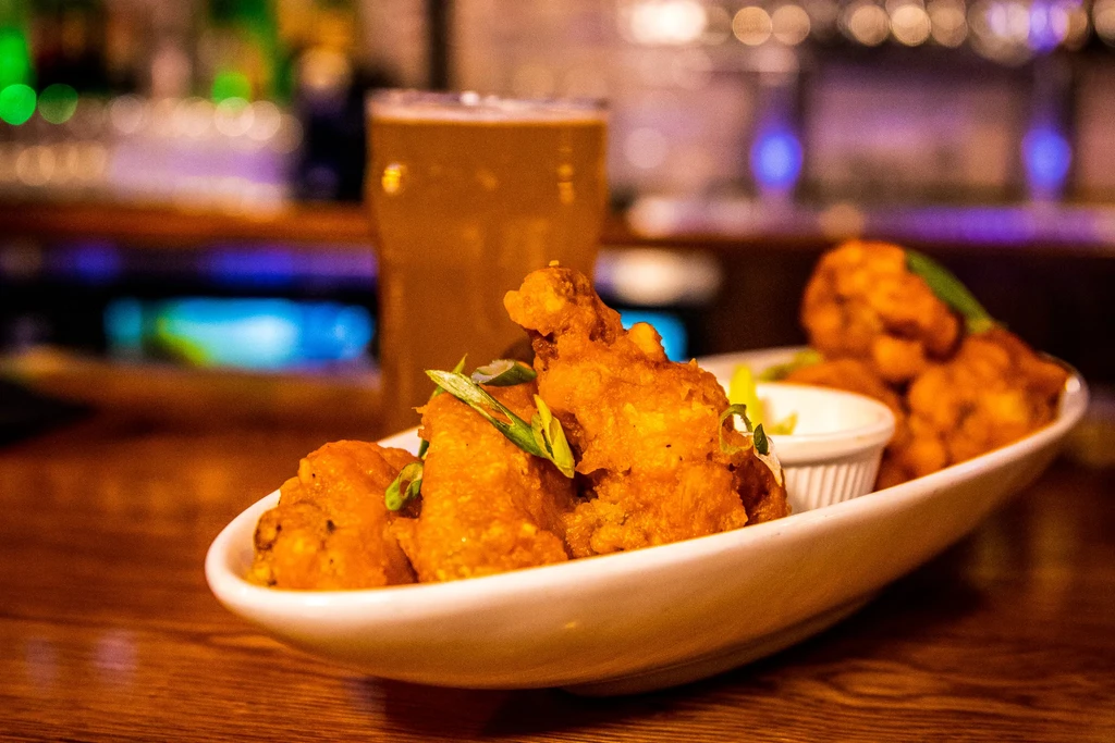Golden-brown fried wings, green onions, dipping sauce, with beer in background.
