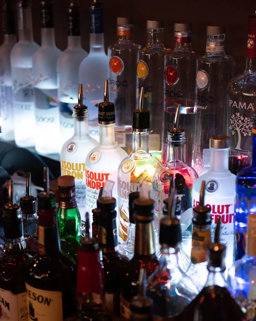 Well-stocked bar shelf displaying various liquor bottles with pour spouts.