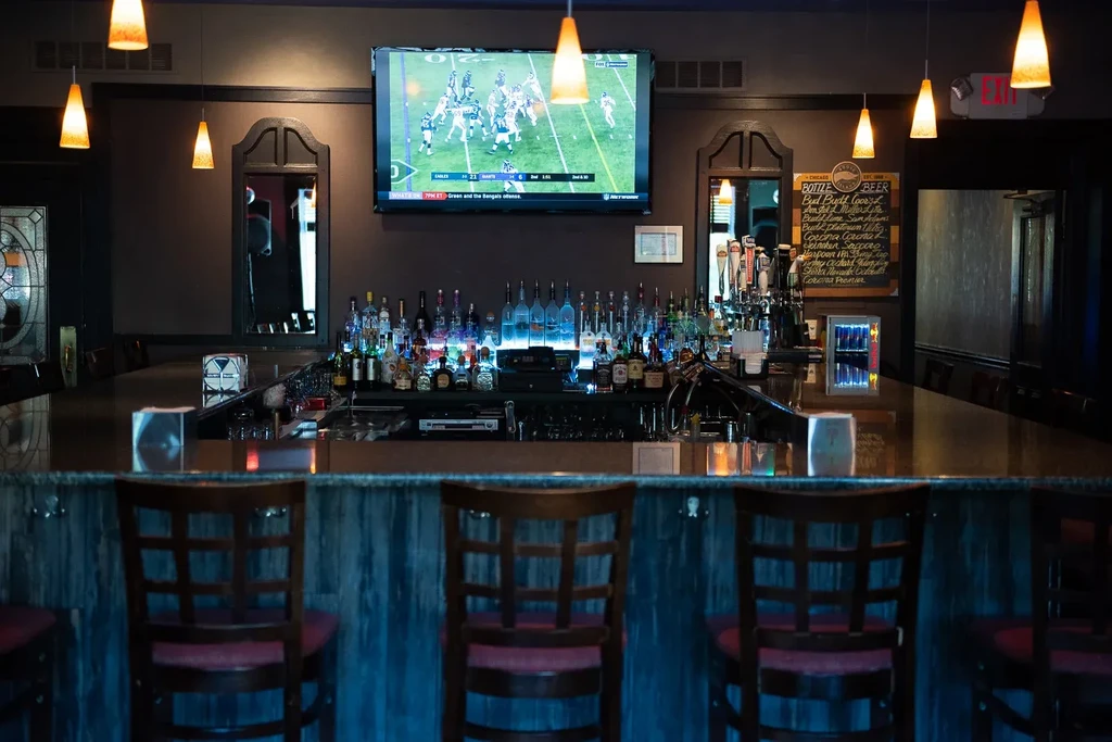 Empty bar stools, blue-lit liquor bottles, and a football game on TV.