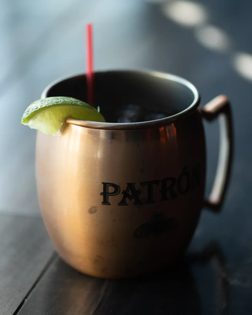 Dark drink in a copper Patrón mug with lime and red straw.