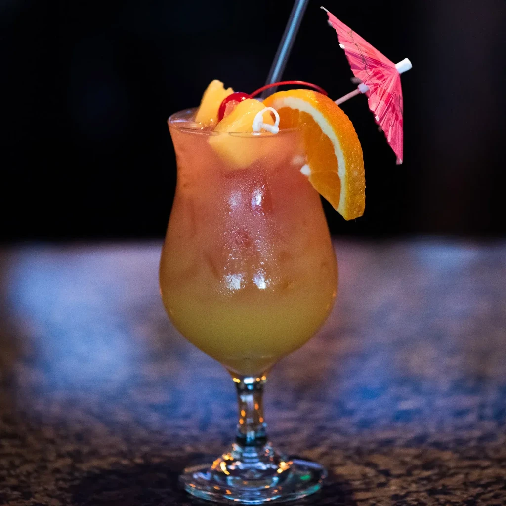 Layered cocktail in frosted glass with fruit and umbrella.