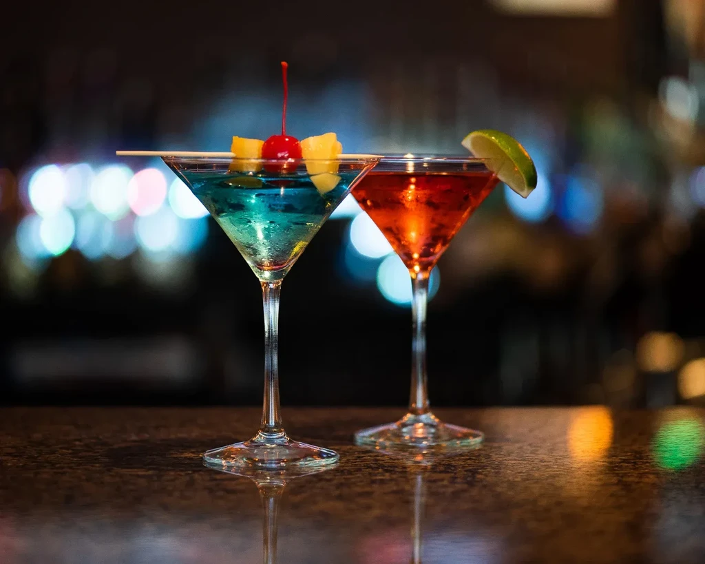 Two blue and red/orange cocktails with garnishes on a reflective bar.