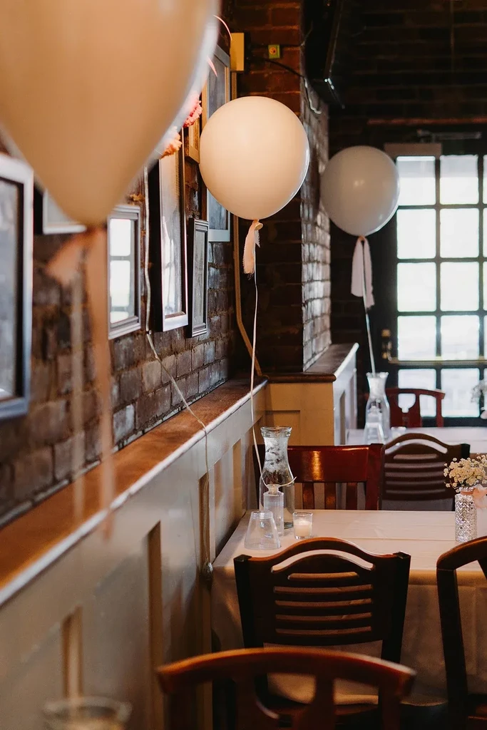 Restaurant interior with white balloons, exposed brick, and a set table.