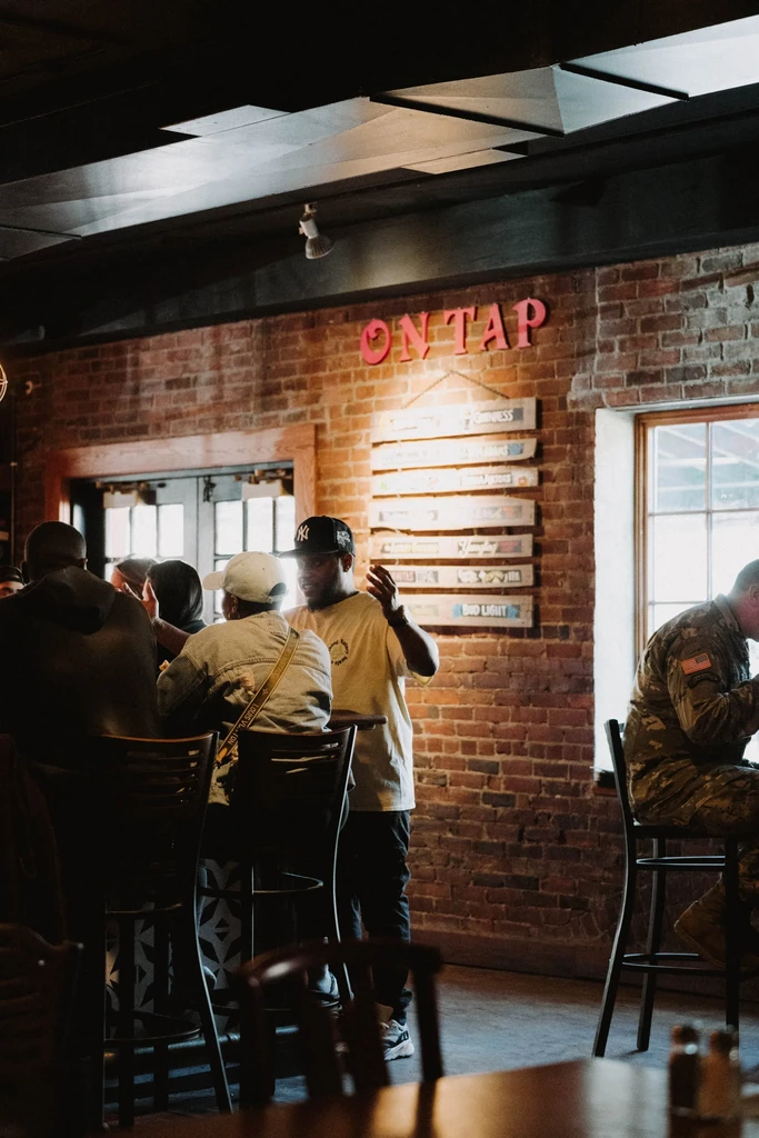 Bar interior with exposed brick, patrons, and prominent "ON TAP" sign.