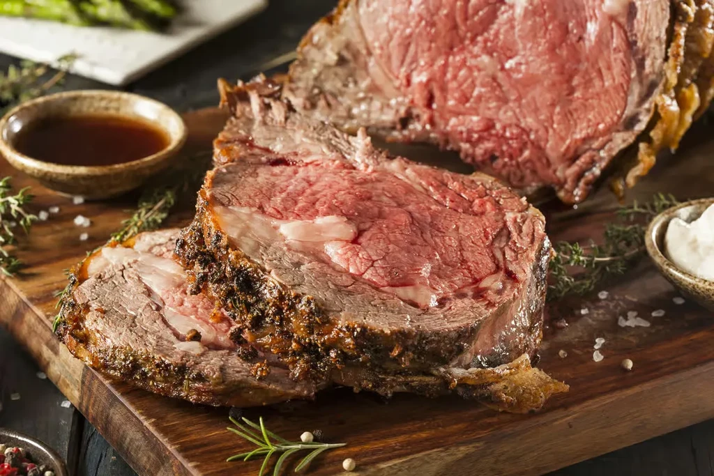 Sliced roasted medium-rare prime rib with sauces and herbs.