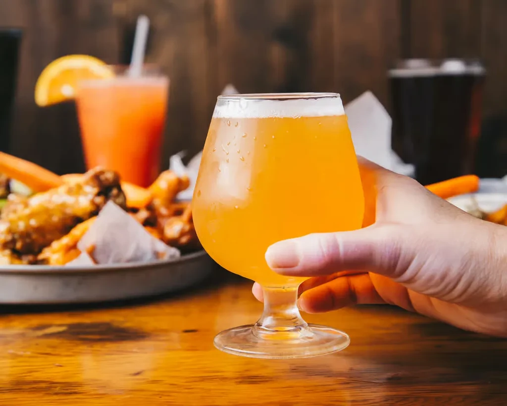 Hand holding frothy beer glass, blurred wings and drinks.