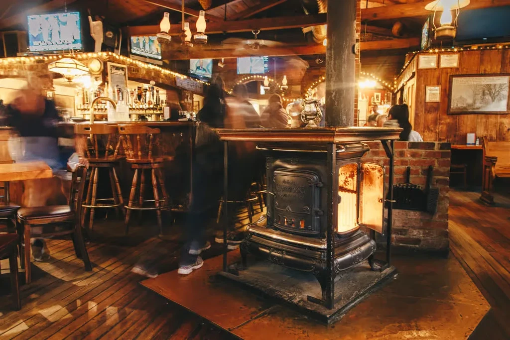 Warm pub interior with glowing wood stove, dark wood, and blurred patrons.