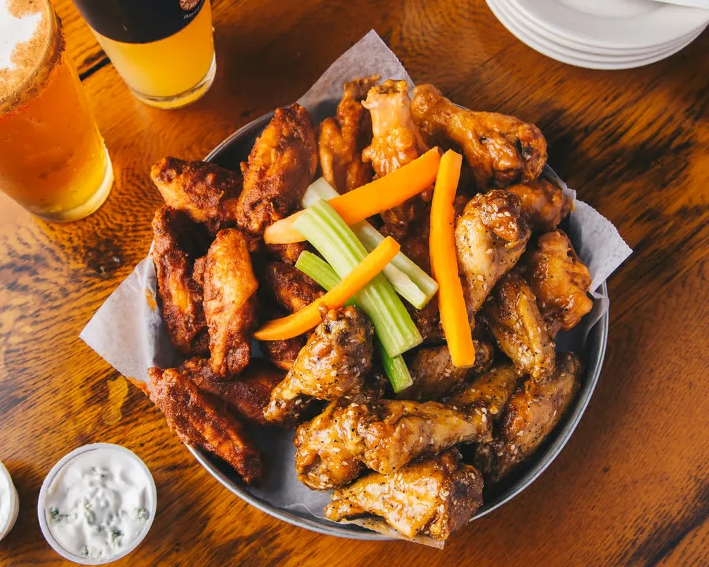 Platter of spicy and glazed chicken wings, dipping sauces, vegetables, and beer.